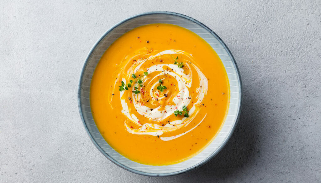 Pumpkin and carrot soup with cream on grey stone background. Top view.