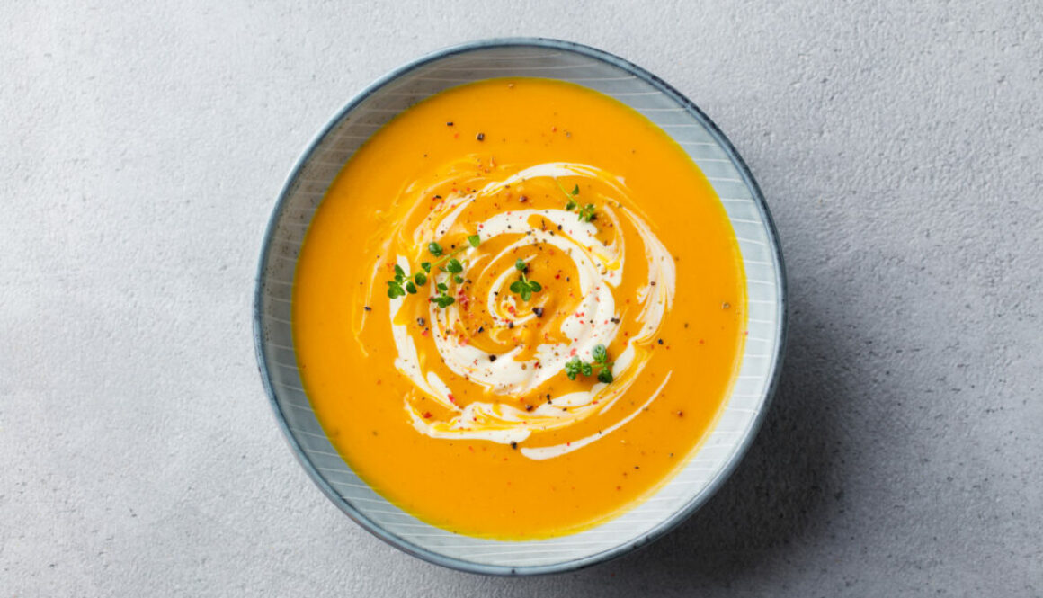 Pumpkin and carrot soup with cream on grey stone background. Top view.